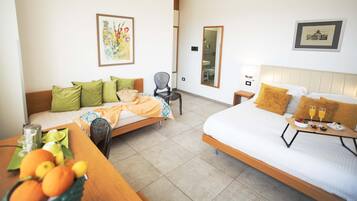 A hotel room with a bed, a sofa, a dining table with fruit, and framed pictures on the walls.