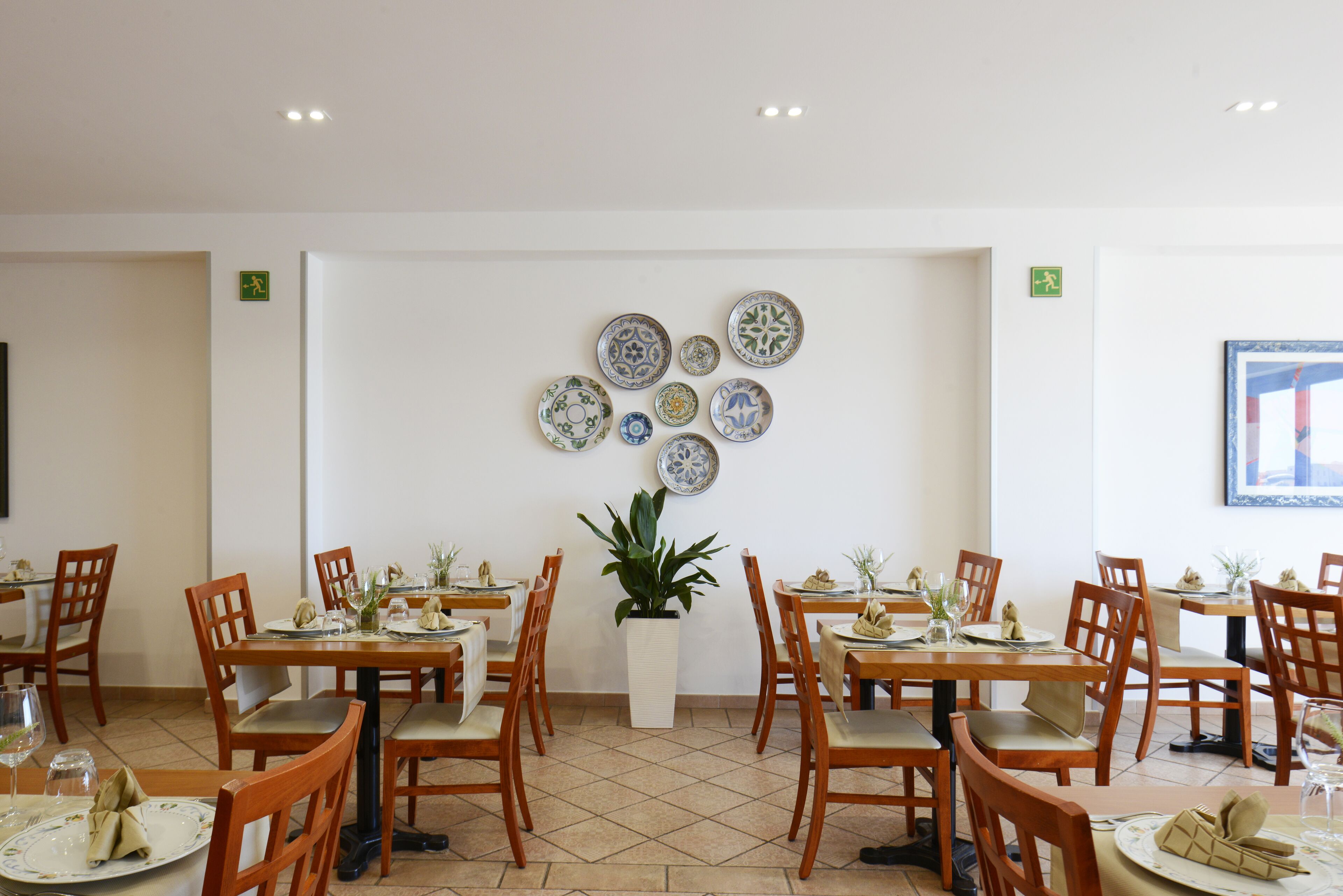 A dining area with multiple tables and chairs, a potted plant, and a wall decorated with plates.
