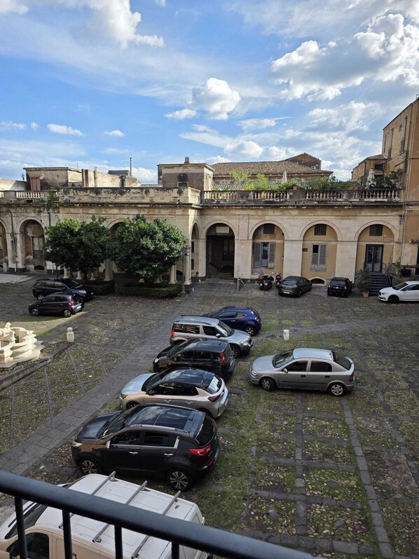 A courtyard with parked cars and a building with arched doorways. - Palazzo Bruca Catania (Catania)