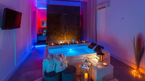 Un cuarto de spa con una bañera grande, velas y un televisor en la pared.