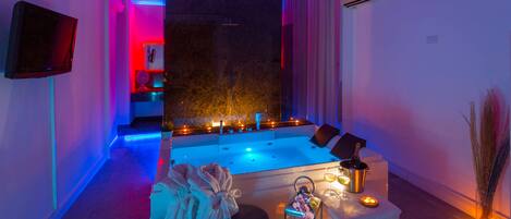 Un cuarto de spa con una bañera grande, velas y un televisor en la pared.
