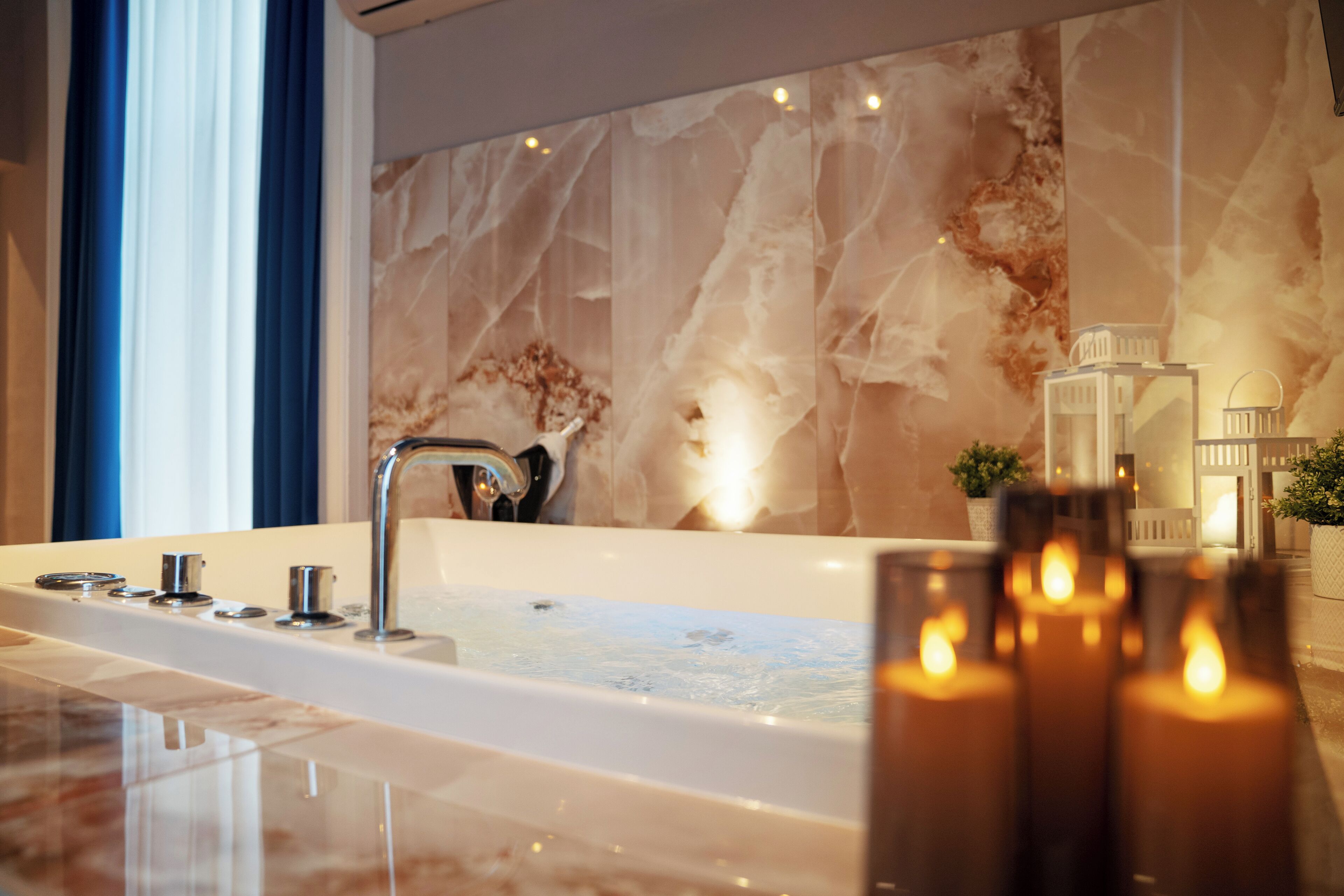 A modern bathroom with a large bathtub, a marble wall, and a small potted plant.