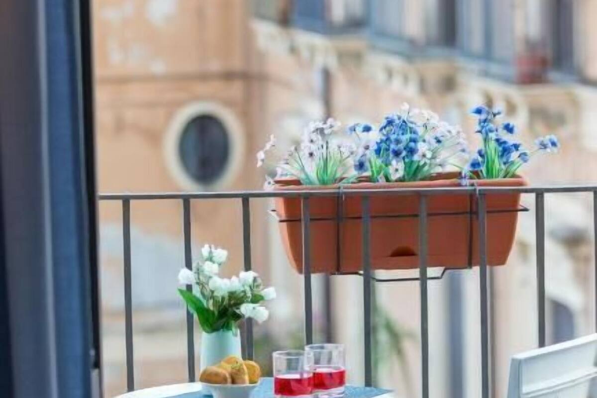 A balcony with a table, chairs, a hanging flower pot, and a view of buildings.