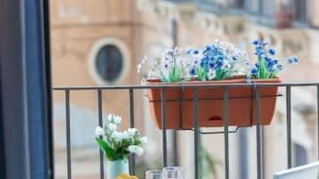 Un balcón con una mesa, sillas, una maceta colgante y vistas a edificios.