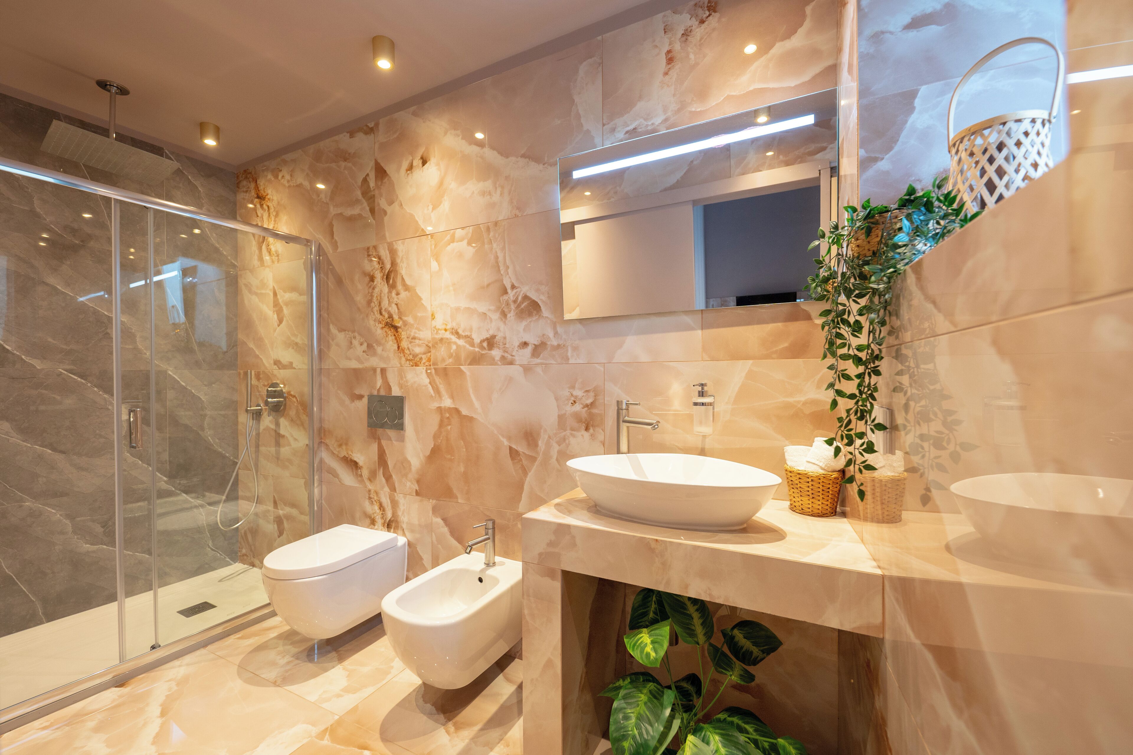 A modern bathroom with a glass-enclosed shower, a bidet, a large sink, and a mirror.