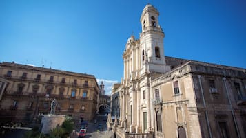 Un edificio histórico con una torre de campanas, una estatua en su fachada y una calle con coches y peatones.