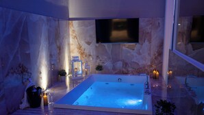 Un baño moderno con una bañera amplia, paredes de mármol, un televisor de pantalla plana e iluminación ambiental.