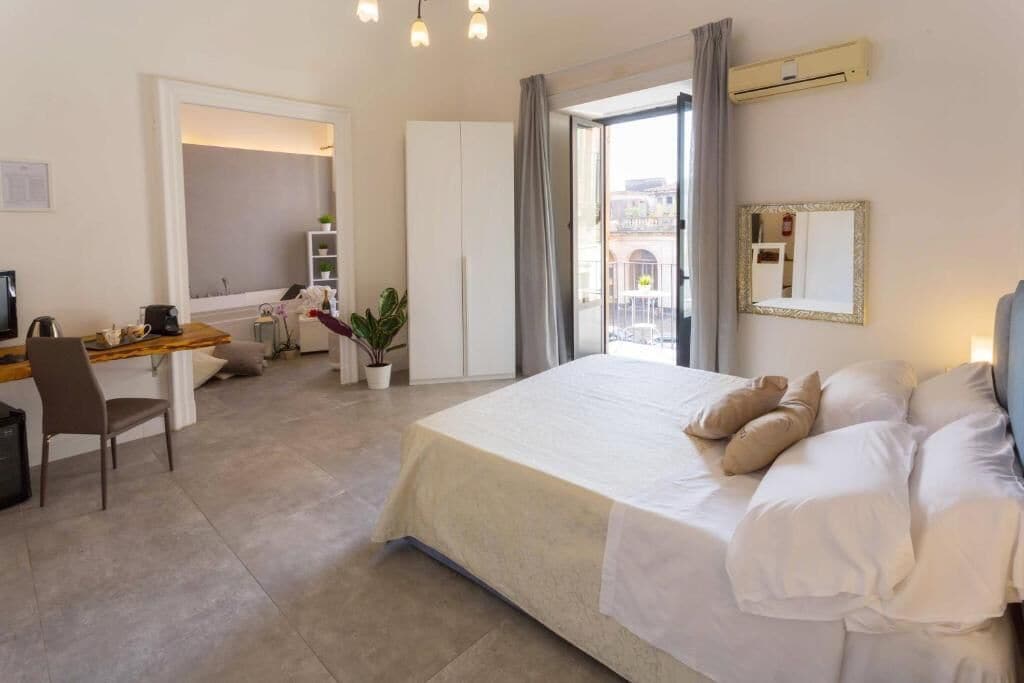 Une chambre d’hôtel avec un lit, un bureau, une chaise, une plante en pot et une fenêtre donnant sur un paysage agréable.