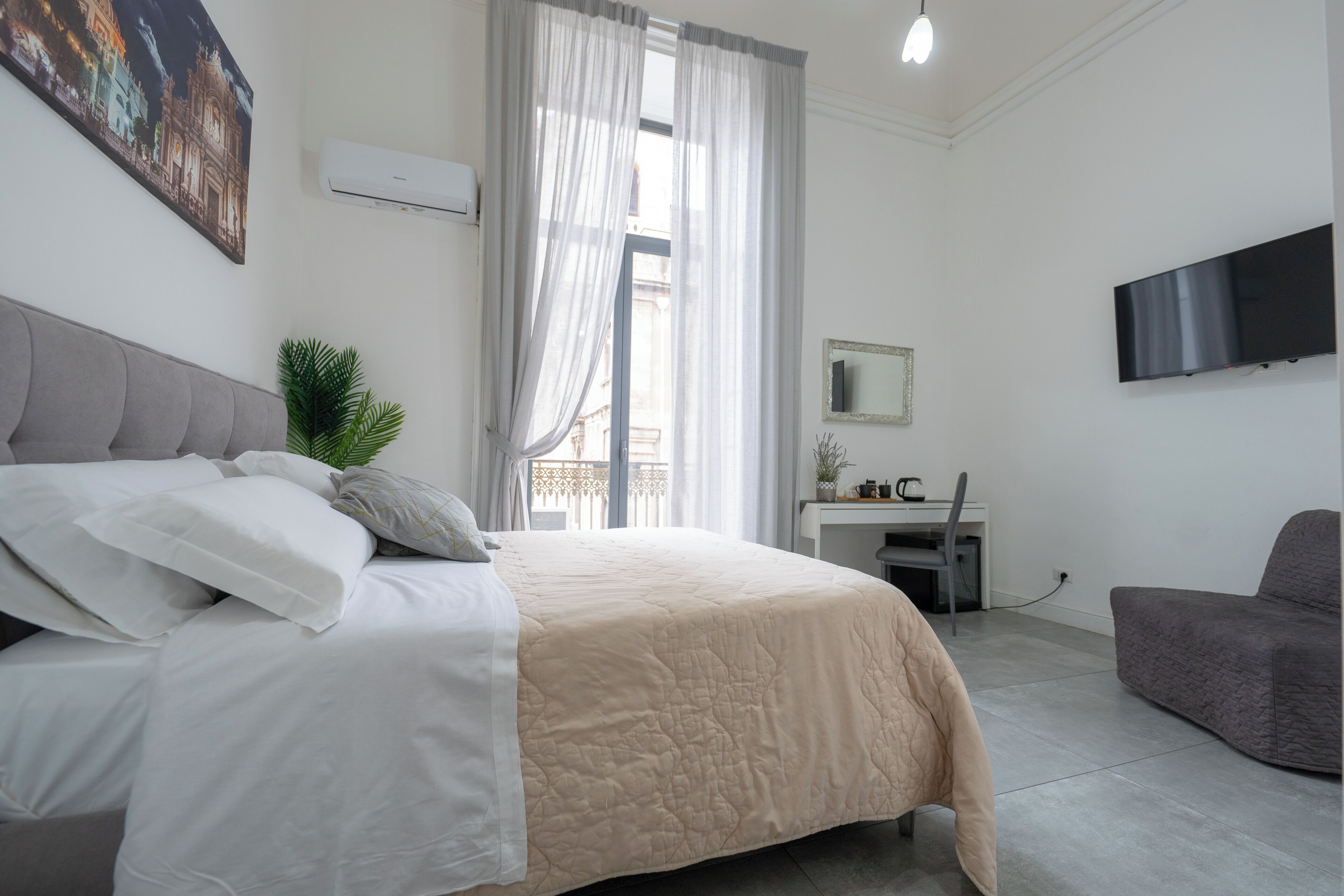 A bedroom with a bed, a desk, a chair, a TV, and a window with curtains.