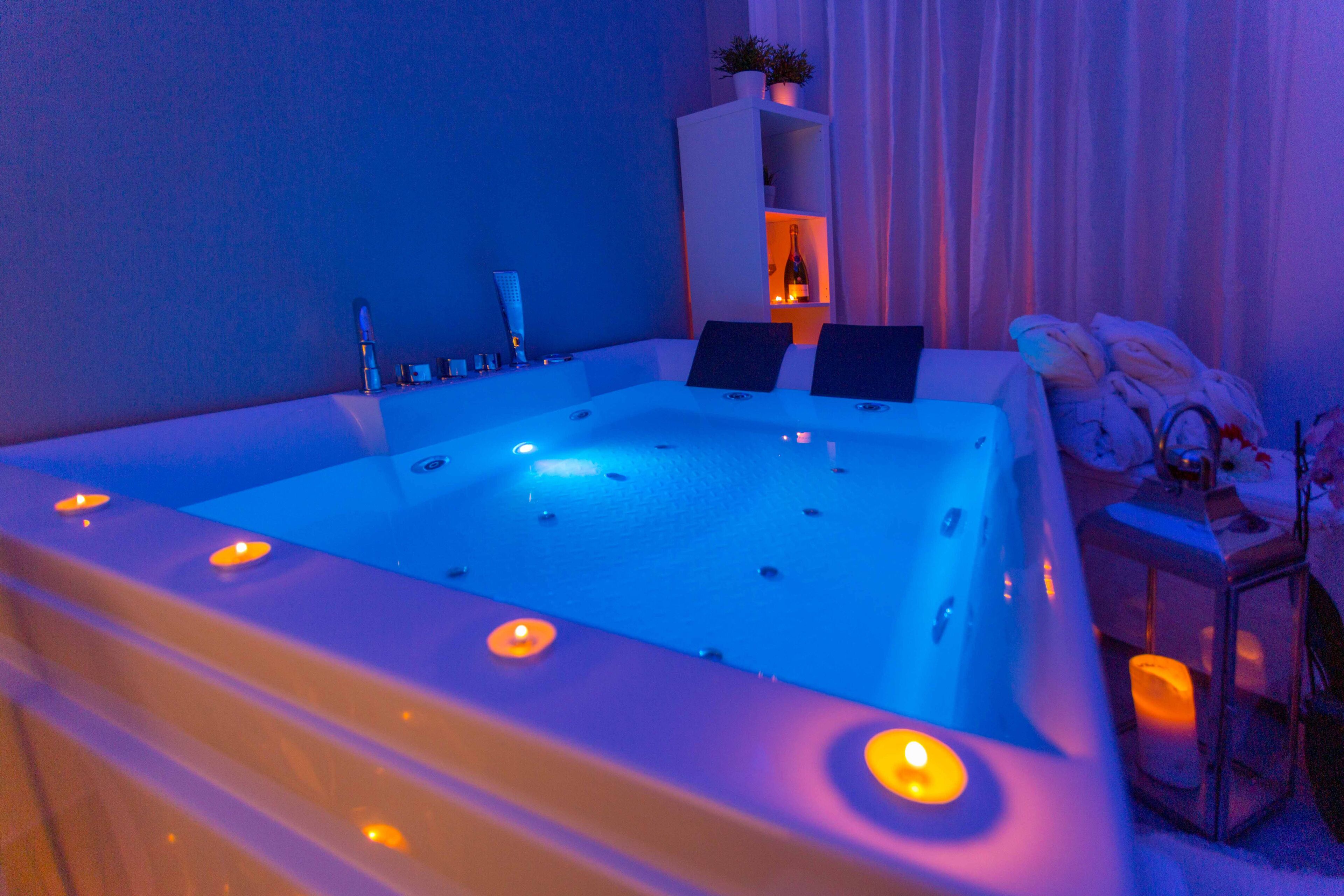 A spa bath with a white tub, candles, and a shelf with a bottle and a plant.