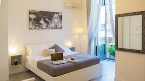 Un dormitorio moderno con una cama, una computadora portátil, una mesita de noche con una lámpara y un cuadro de un paisaje urbano en la pared.