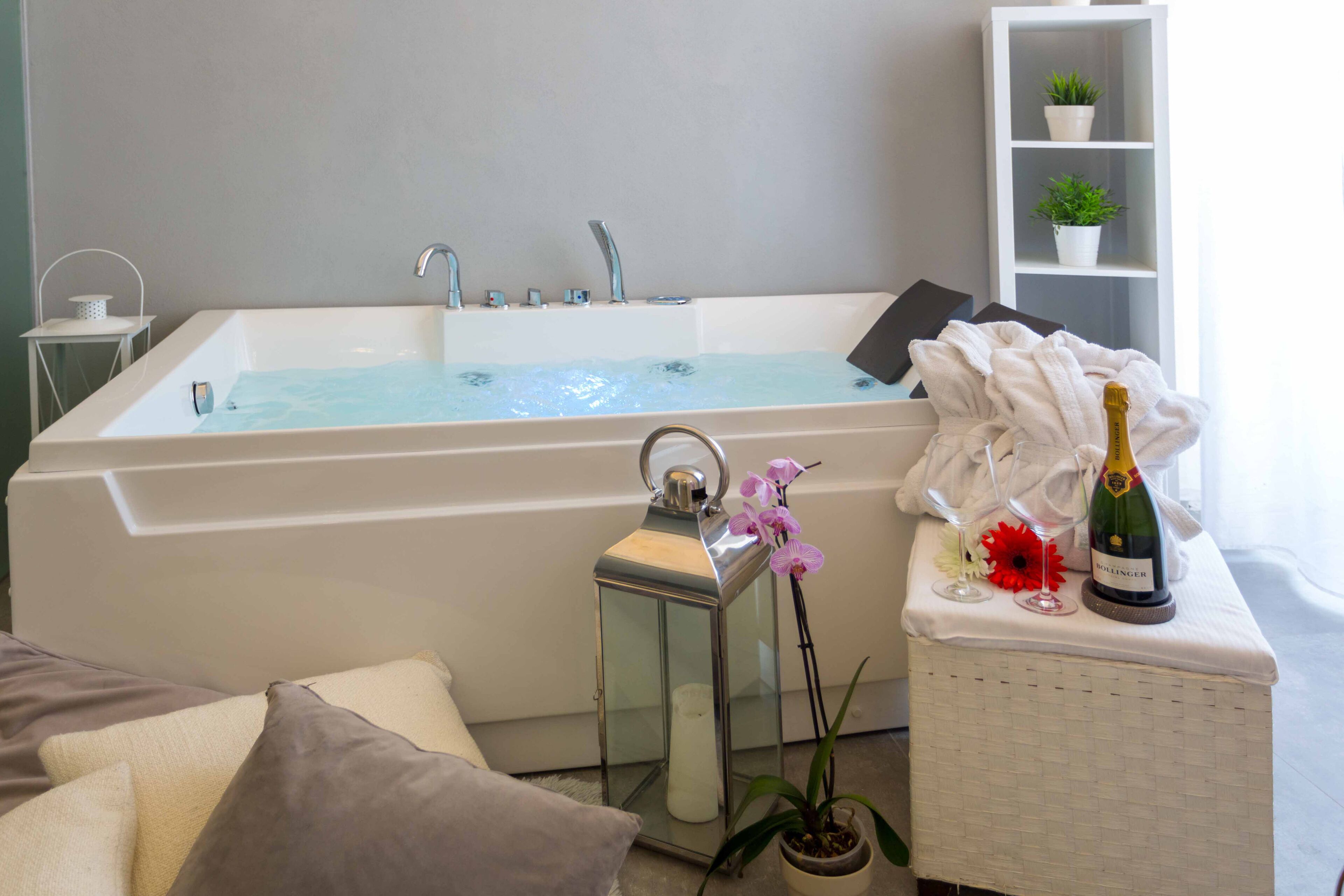 Un baño moderno con una bañera grande, una pequeña mesa con una botella de champán, una orquídea en maceta y una vela.