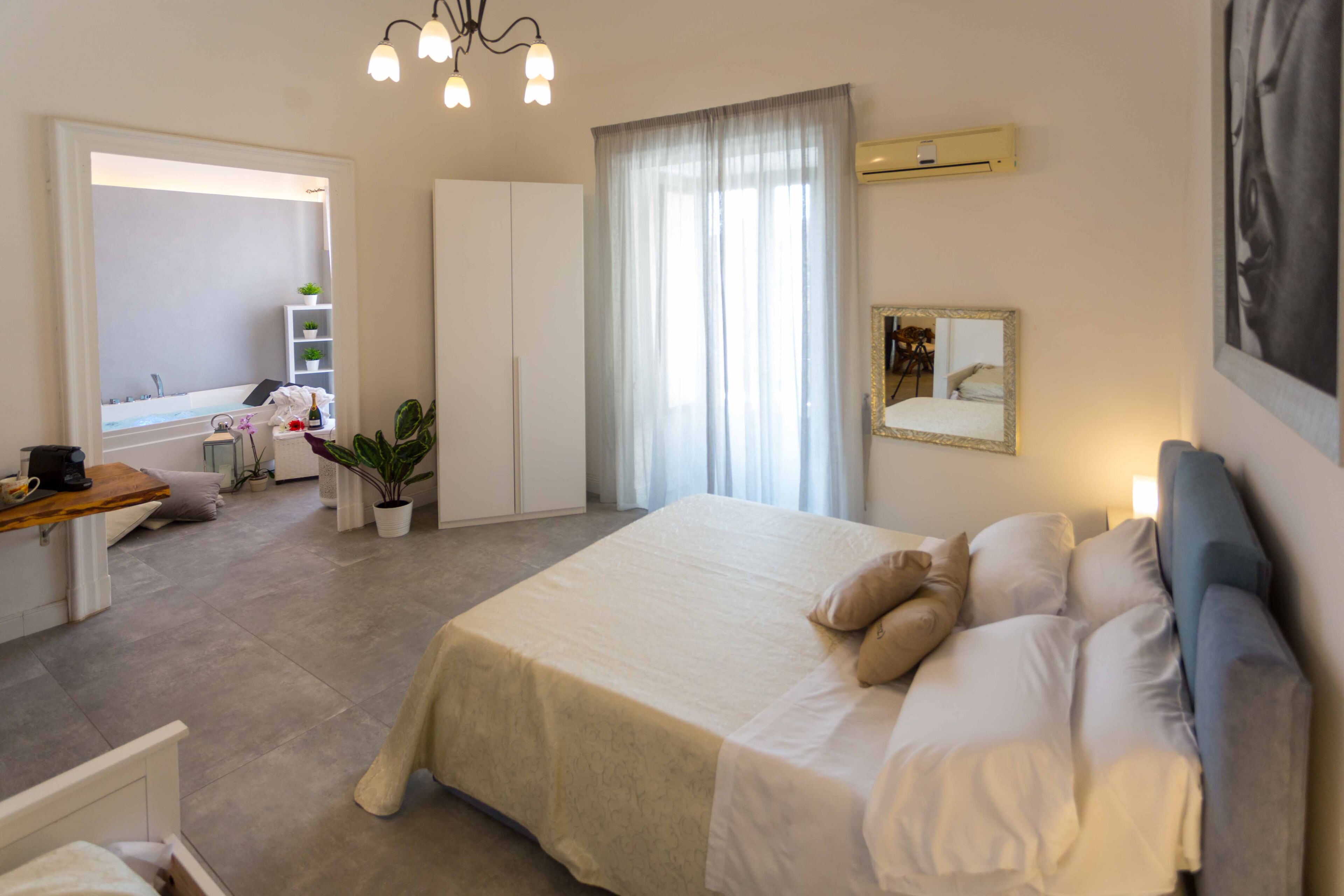 Une chambre d’hôtel comprenant un lit, un bureau, une chaise, une plante en pot, une armoire et une fenêtre avec des rideaux.