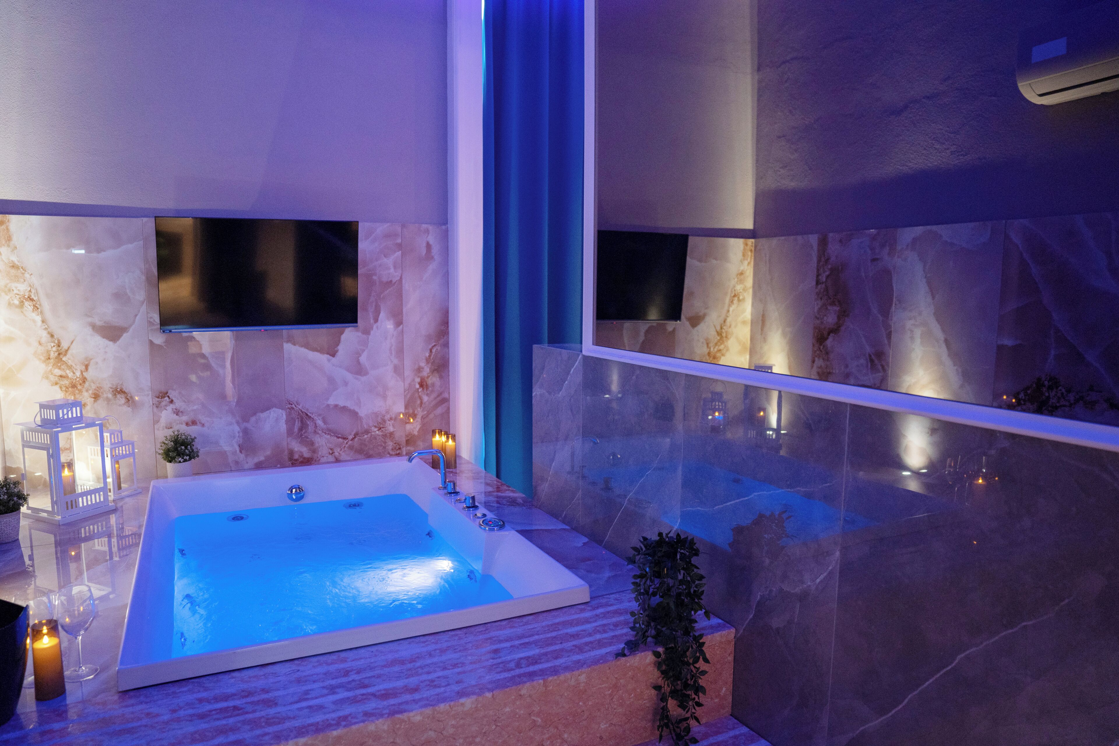 A modern bathroom with a large bathtub, marble walls, and a flat-screen TV mounted above it.
