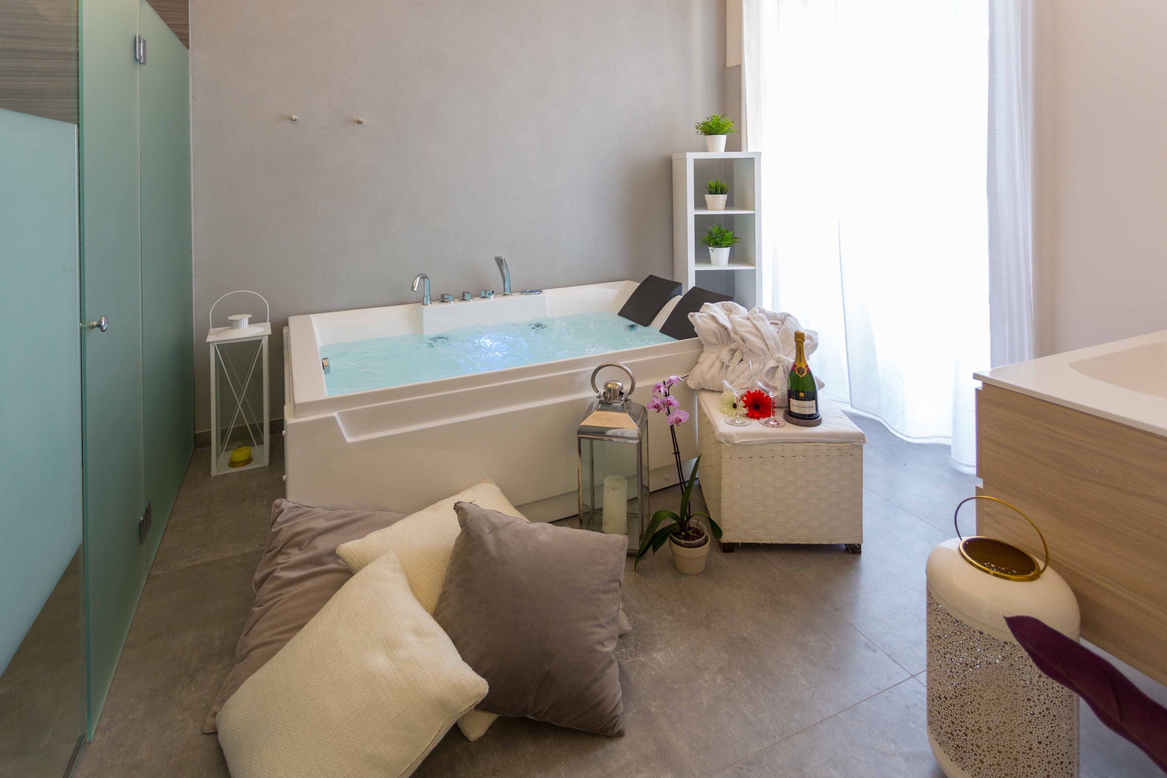 Un bagno moderno con una vasca, un tavolino con una pianta, uno scaffale con piante e una bottiglia di champagne.