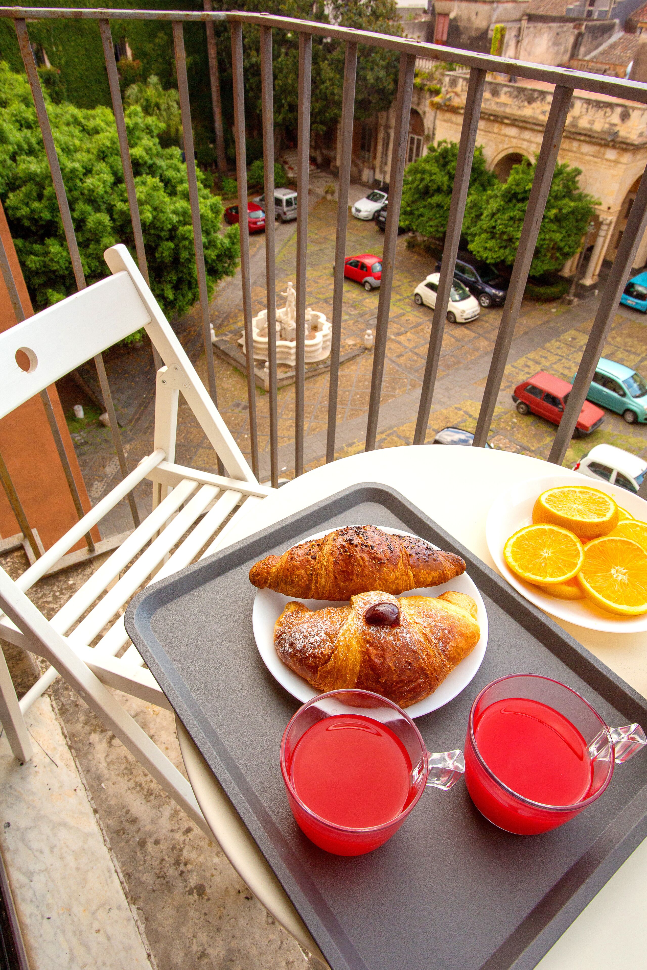 A balcony with a tray of croissants, orange slices, and two glasses of red drink.