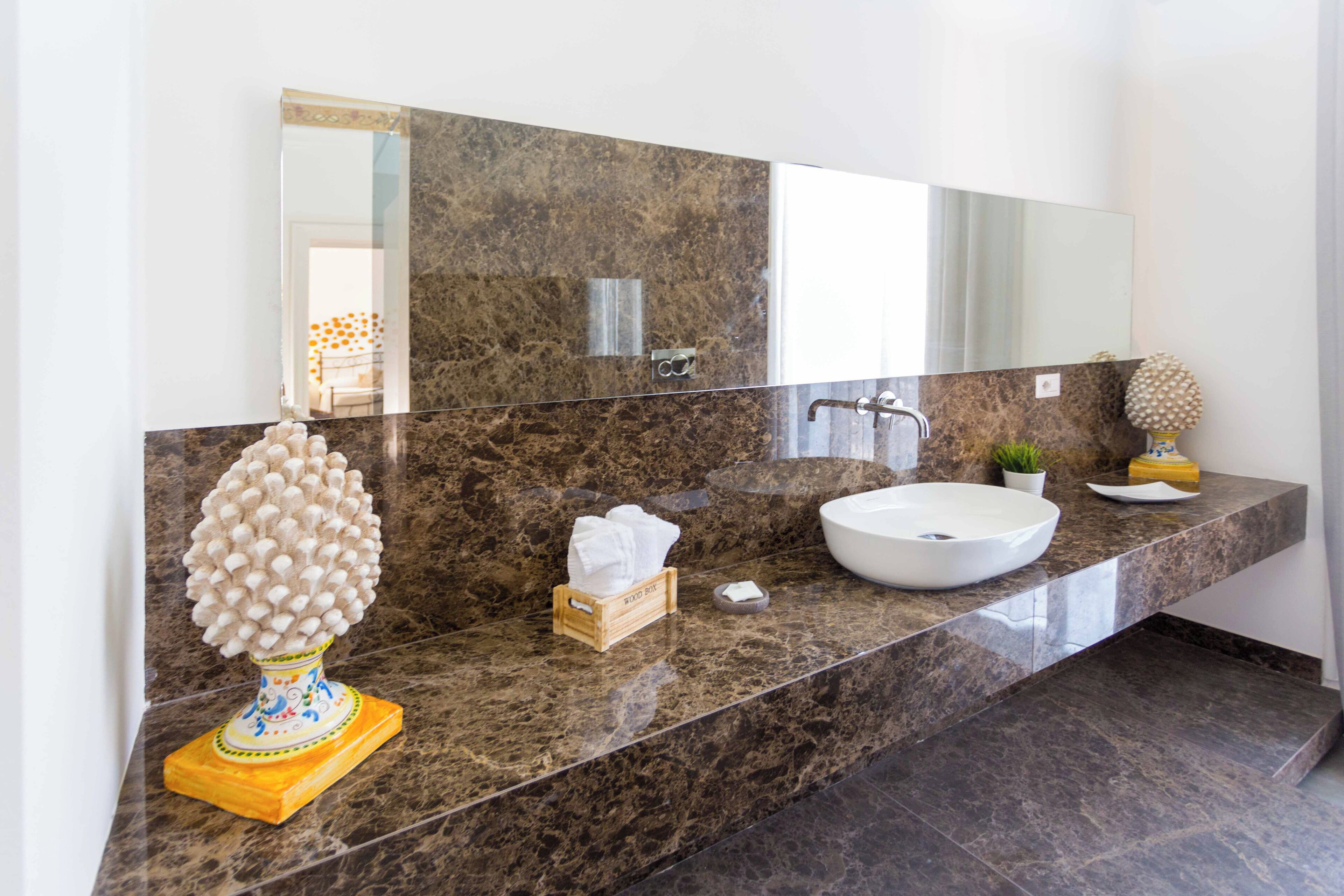 A modern bathroom with a marble countertop, a white sink, a large mirror, and a decorative tree sculpture.