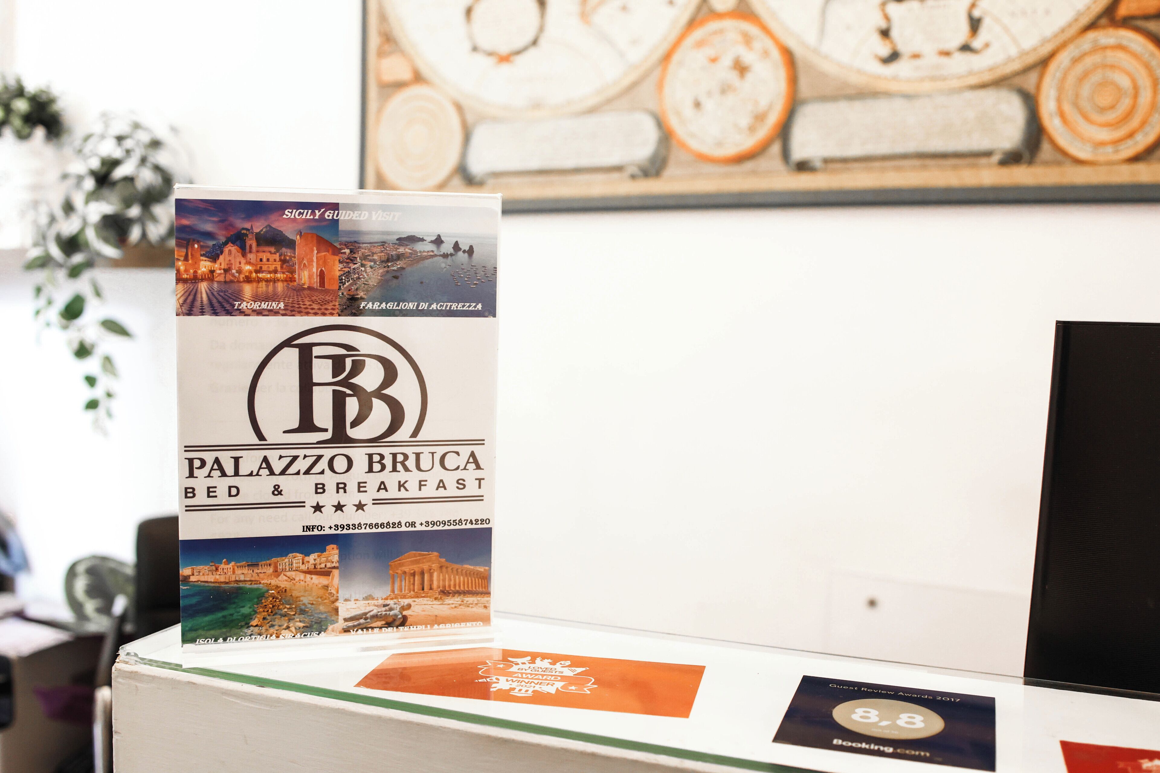 Une enseigne indiquant le « Palazzo Bruca Bed & Breakfast », avec une vue panoramique sur une ville côtière.