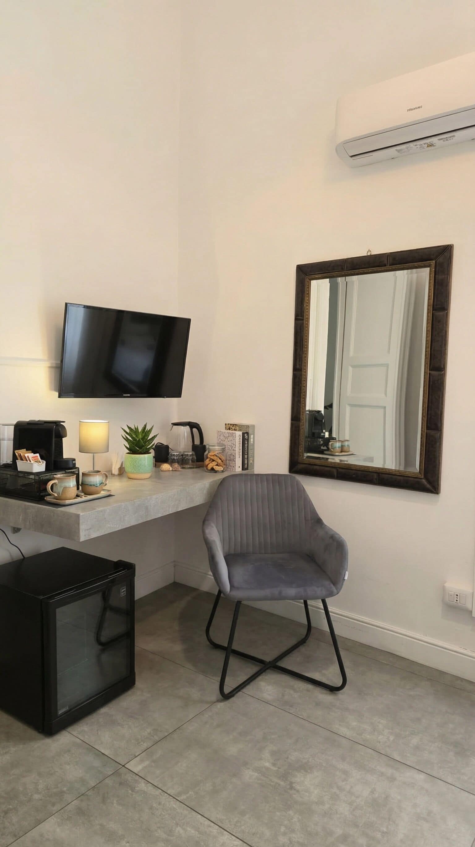 A modern room with a flat-screen TV mounted on the wall, a desk with a lamp, a chair, and a small black cabinet.