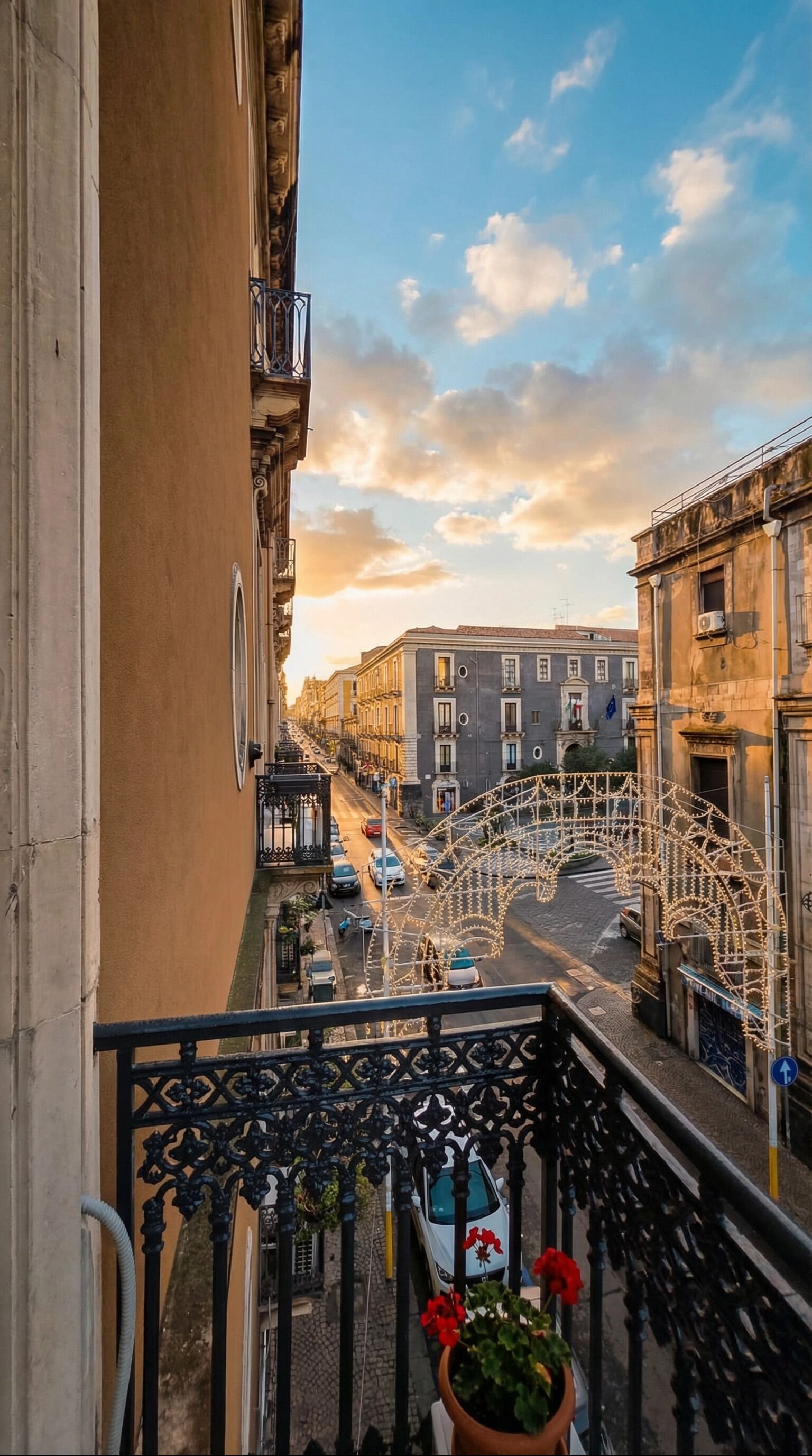 Ein Balkon mit Blick auf eine straße, gesäumt von Gebäuden, einem Zierbogen und einem Blumentopf mit Blumen.