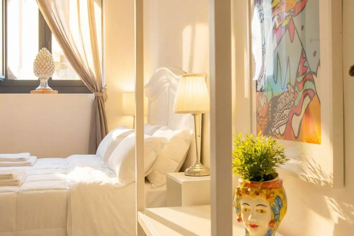 A hotel room with a bed, bedside table, lamp, and a colorful vase.