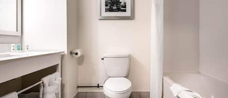 A modern bathroom with a toilet, a framed picture on the wall, a bathtub, and a shelf with towels.