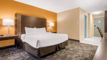 Una habitación de hotel con una cama grande, dos lámparas de noche, un cabecero de madera y suelo alfombrado.