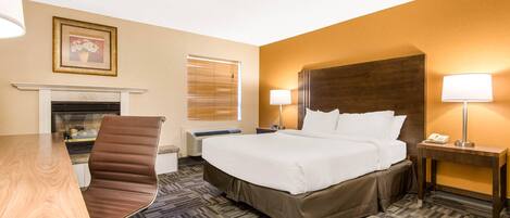A hotel room with a bed, a desk, a chair, a fireplace, and two bedside lamps.