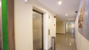 A hallway with a metallic elevator, a trash bin, and a wall-mounted fire alarm. - Hotel Westree (Kuala Lumpur)