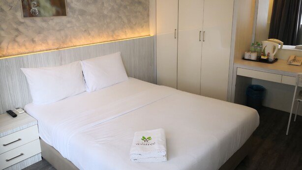 A neatly made bed with a folded towel, a bedside phone, and a desk with a mirror and a coffee maker. - Hotel Westree (Kuala Lumpur)