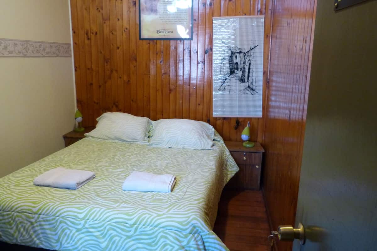 A wooden-paneled room with a bed, two pillows, a framed certificate, and a lamp on a nightstand.