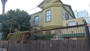 A two-story house with a green facade, a black metal fence, and a 'NO ESTO' sign.