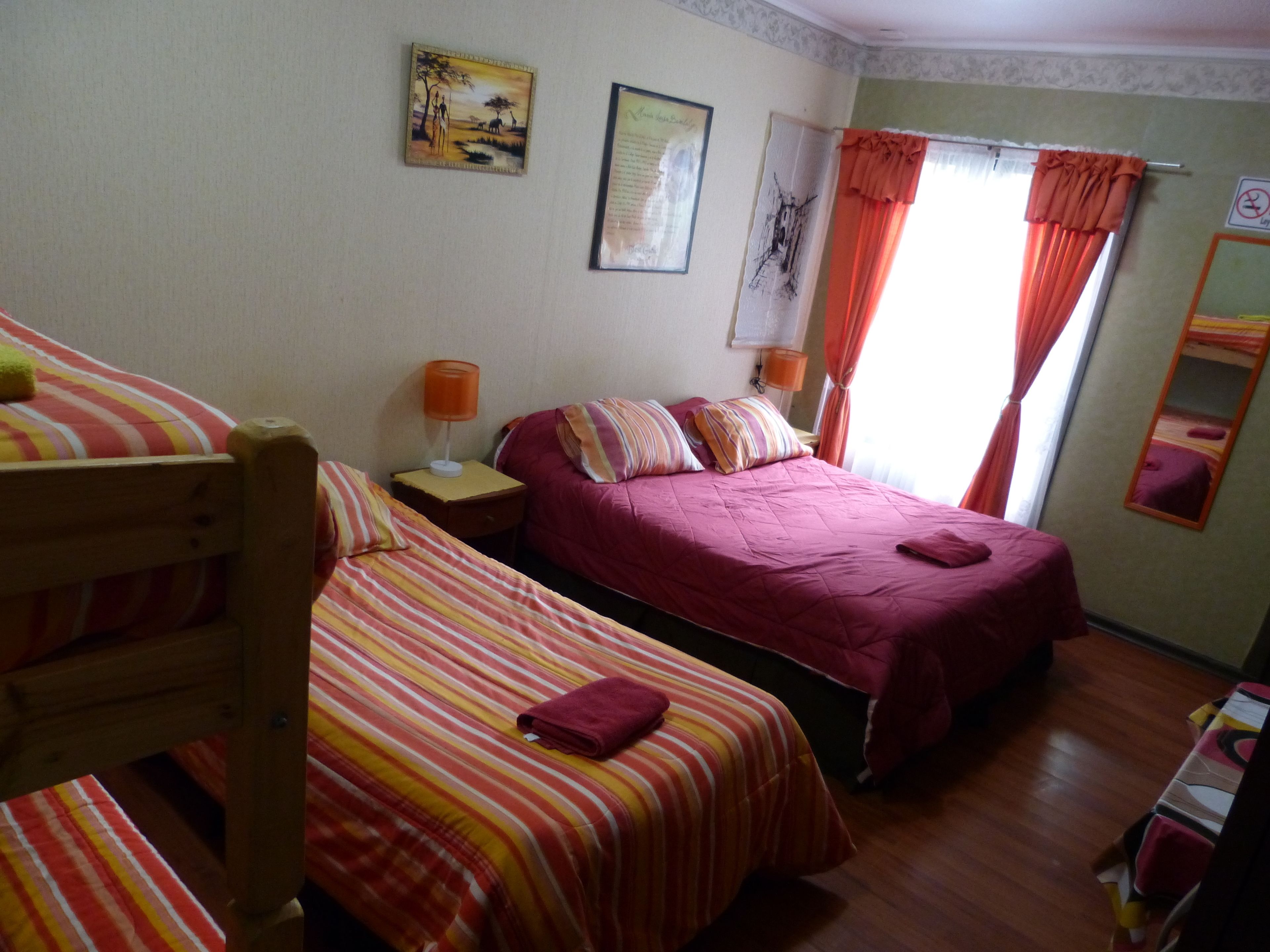 A room with two single beds, a nightstand with a lamp, a painting on the wall, and a window with curtains.