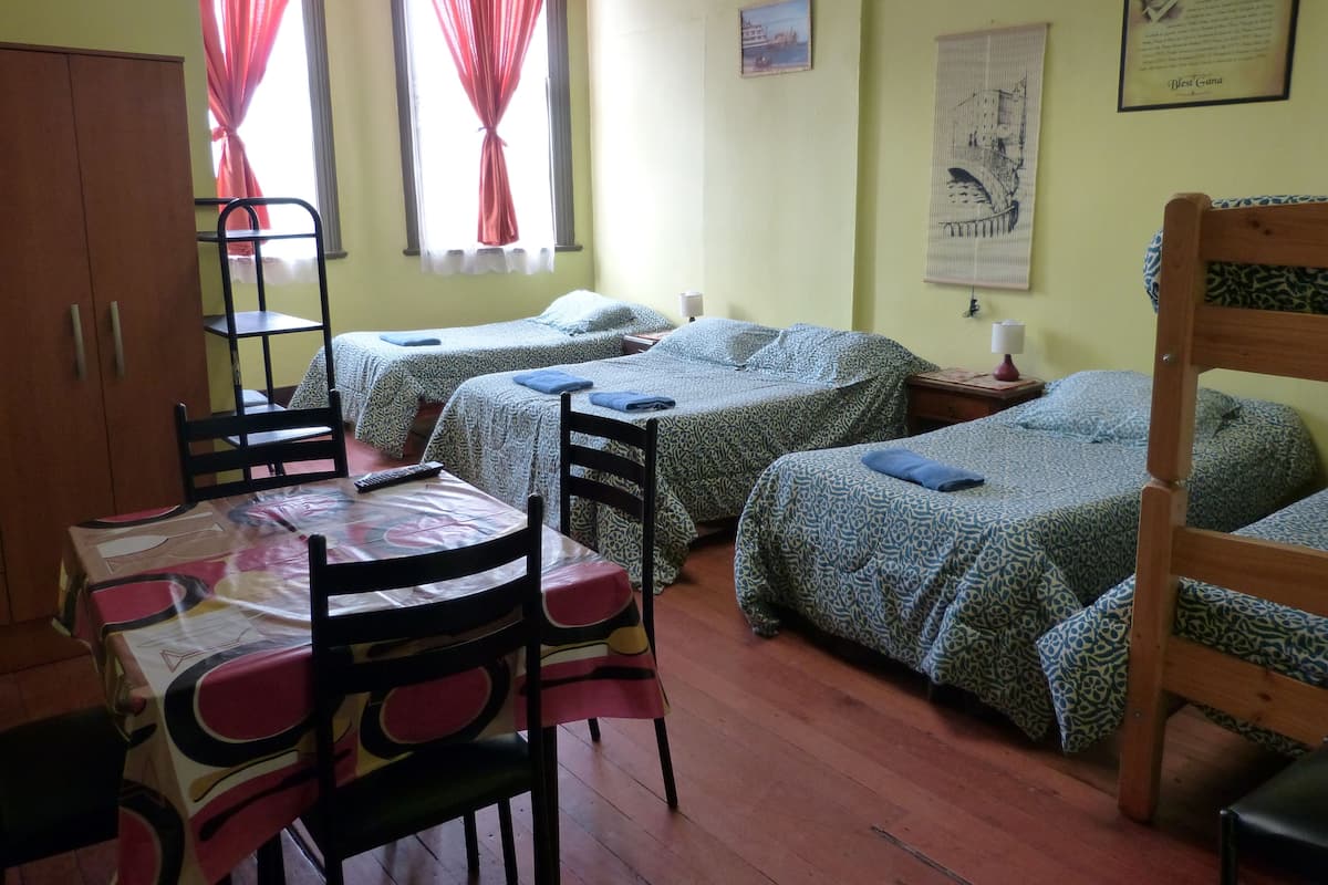 A room with two beds, a table with chairs, a wardrobe, and a window with curtains.
