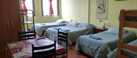 A room with two beds, a table with chairs, a wardrobe, and a window with curtains.
