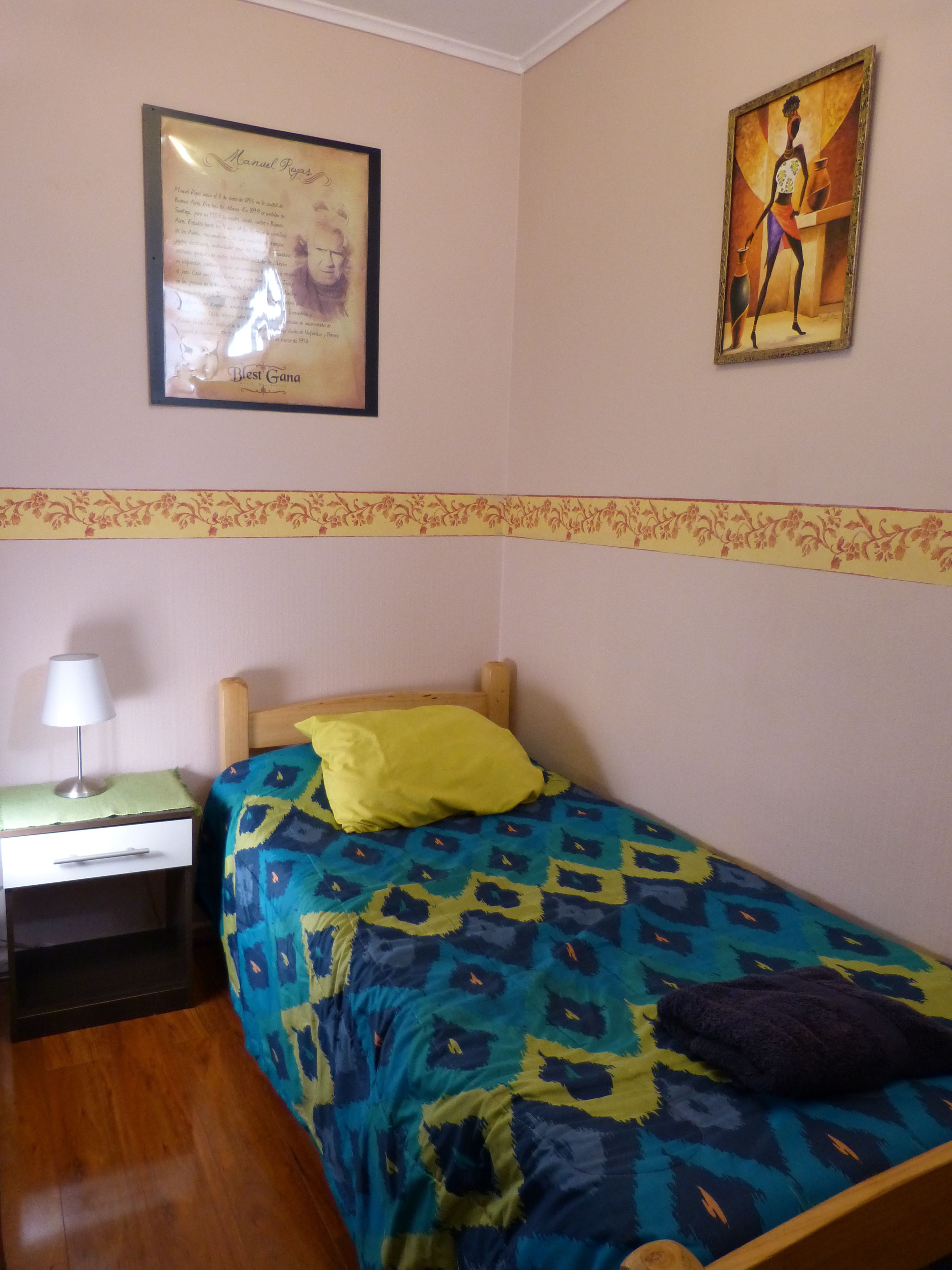 A bedroom with a bed, a nightstand, a lamp, and two framed artworks on the wall.