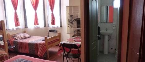 A bedroom with two beds, a desk, and a bathroom visible through an open door.