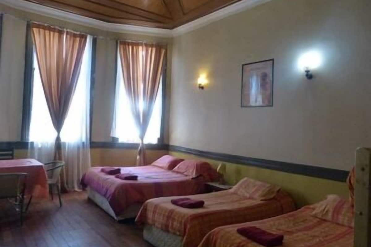 A hotel room with two single beds, a small table, and a chair.