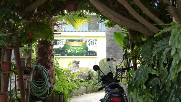 A motorcycle parked under a tree, with a sign for 'Hostal Residencia Blest Gana' in the background.