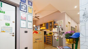 Una habitación de hotel con puerta de madera, kitchenette, ventilador de techo y una silla con un libro.