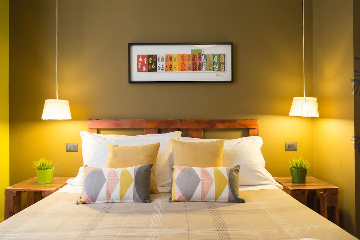 A neatly made bed with two pillows, a framed artwork above, and two bedside tables with lamps and plants.