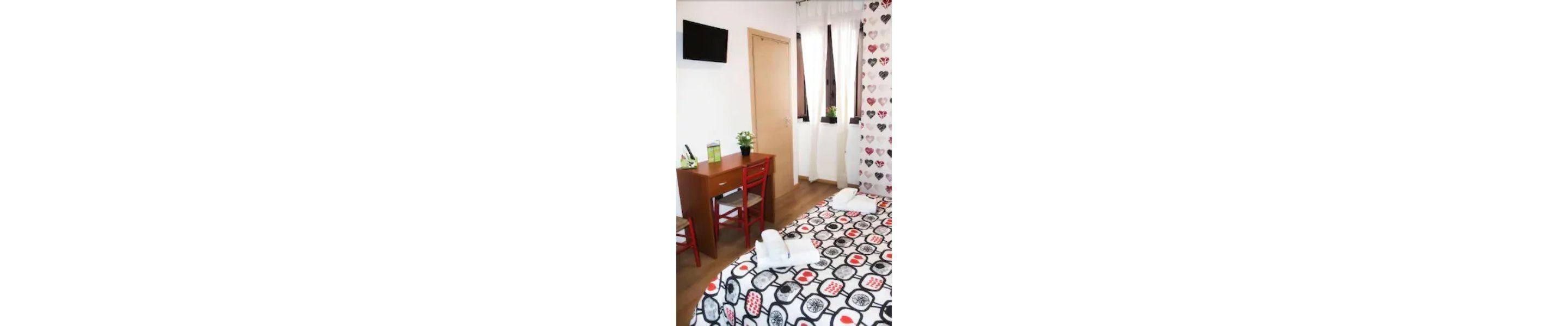 A room with a bed, a desk, and a chair. There is a window with curtains and a door.