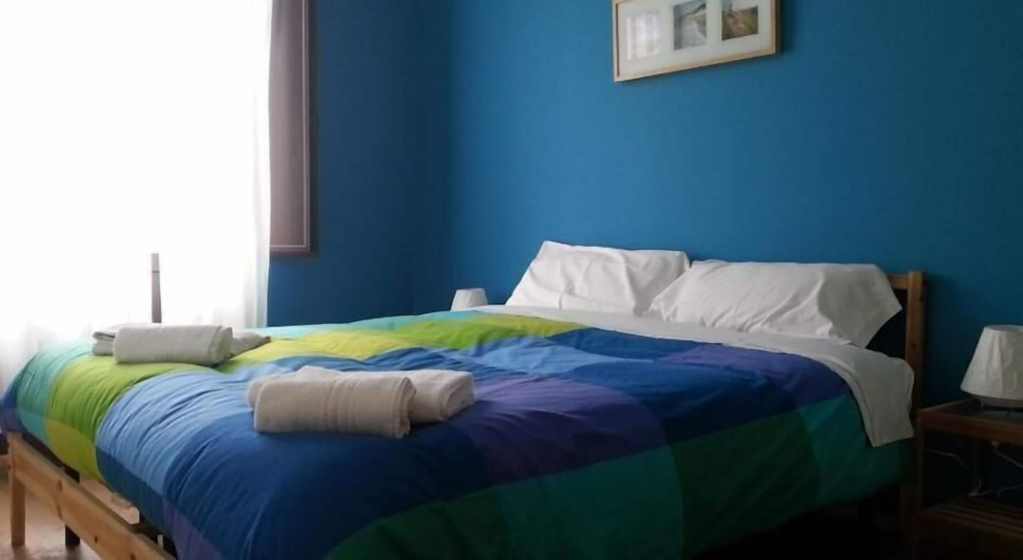 A bed with a colorful quilt, a bedside table with a lamp, and a framed picture on the wall.