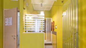 Un pasillo con paredes amarillas, una puerta de madera y un separador de vidrio con diseño de listones blancos.