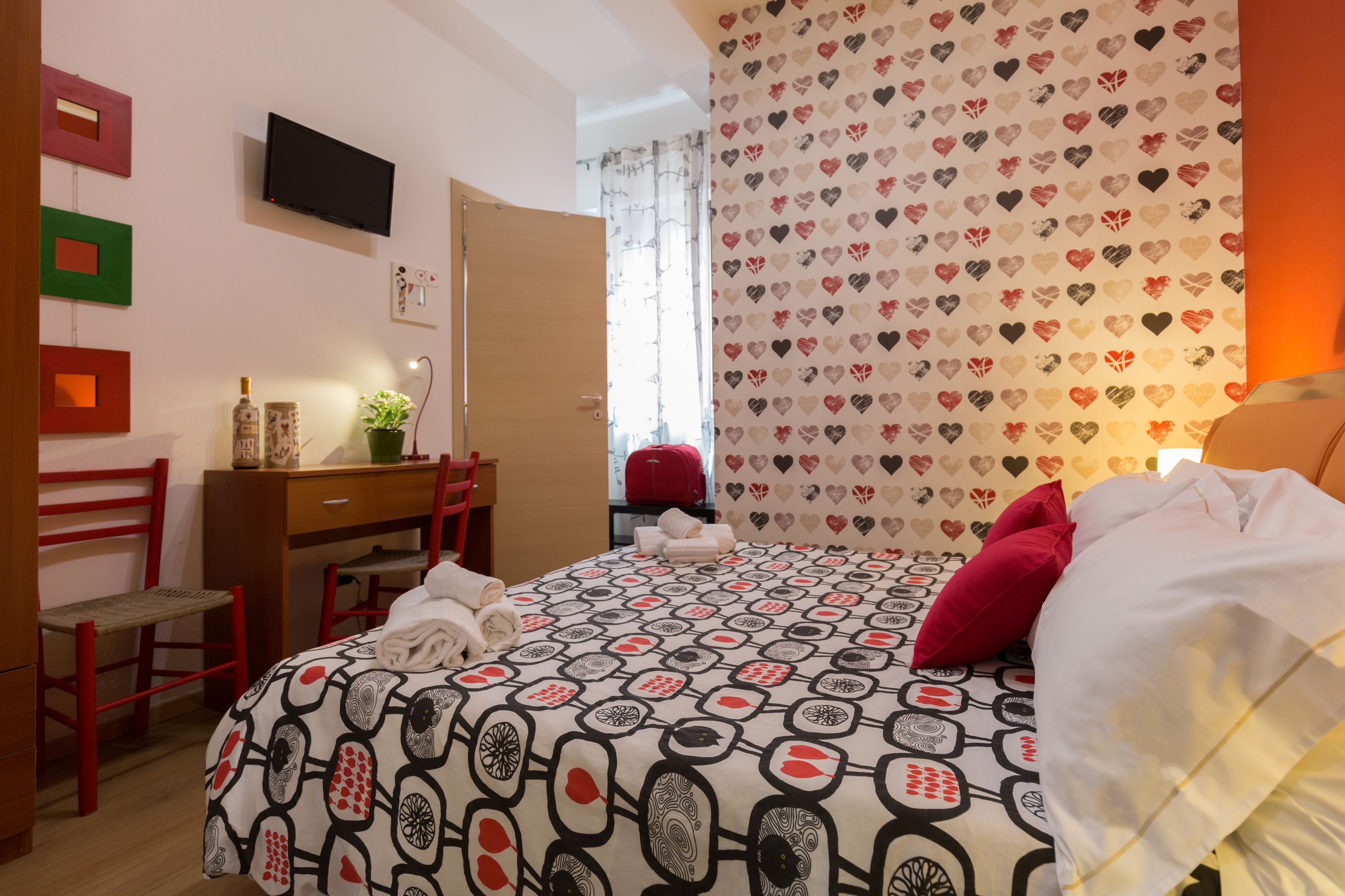 Ein Hotelzimmer mit Bett, Schreibtisch, Stuhl und einem Fernseher an der Wand.