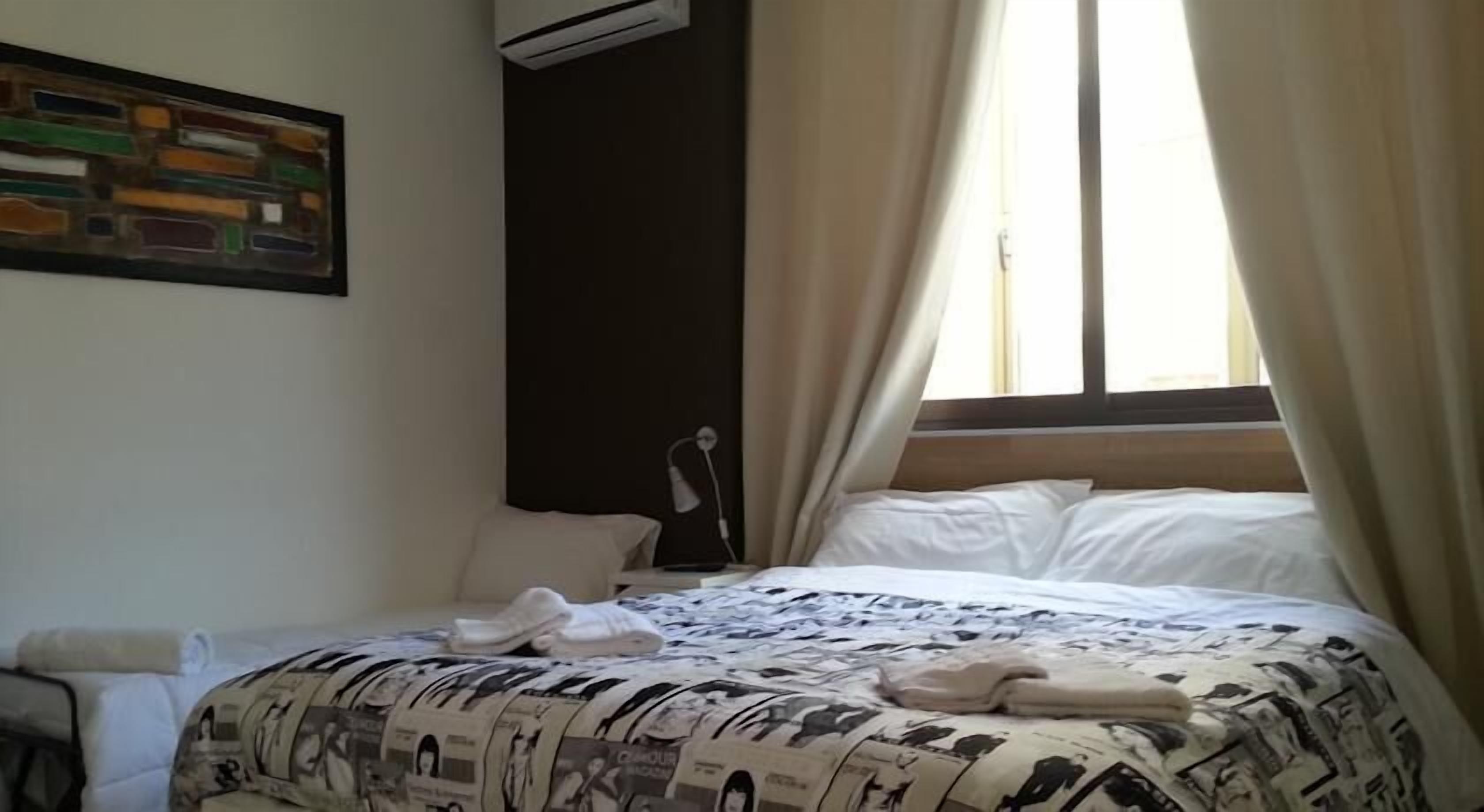 A hotel room with a bed, a nightstand, a lamp, and a painting on the wall.