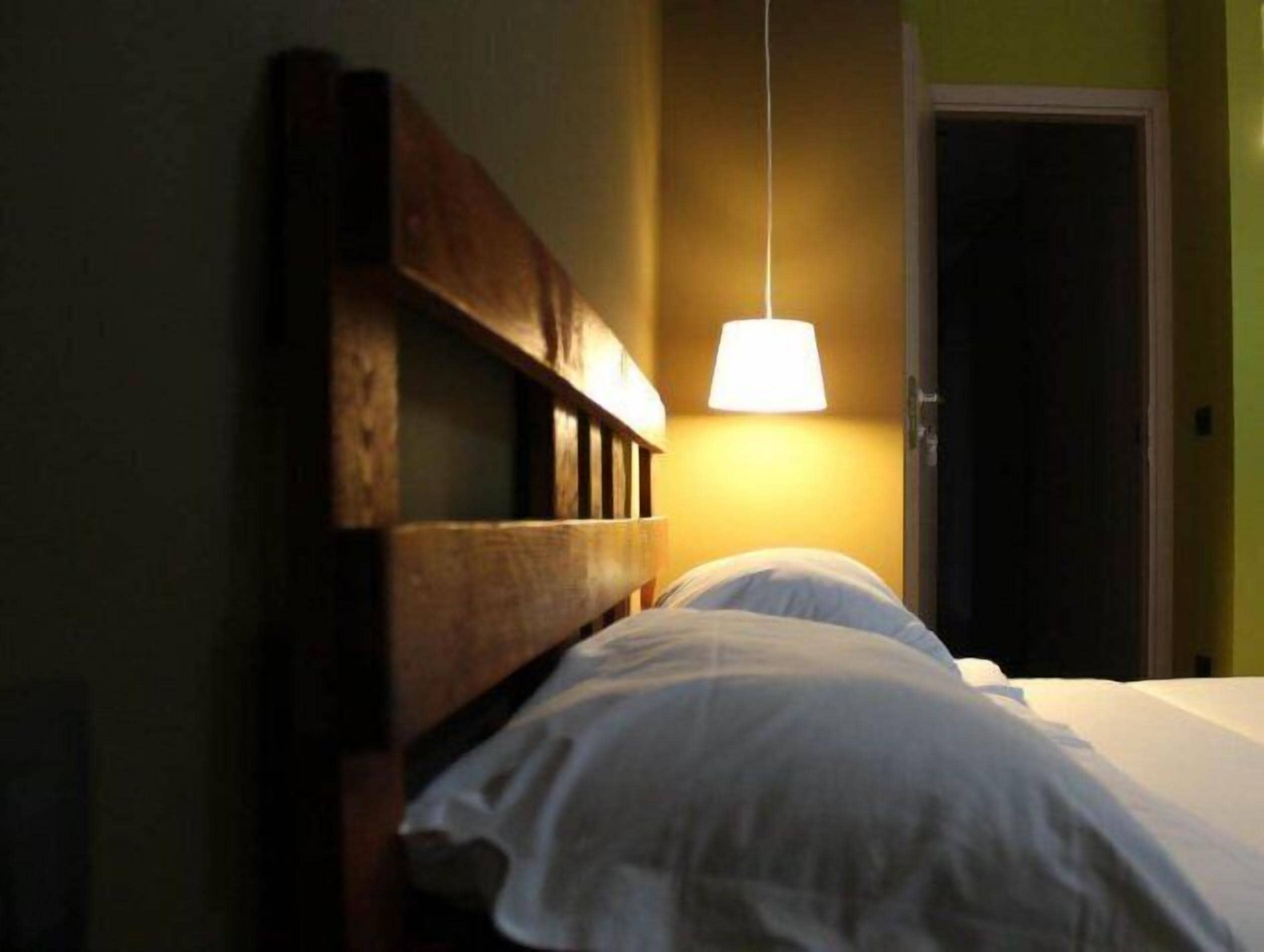 A room with a wooden headboard, a bed with white bedding, and a hanging lamp providing light.