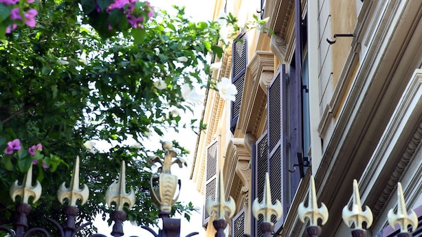 A building facade with ornate metal gates and a tree with pink flowers. - Roma Room Hotel (Rome)