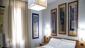 A hotel room with a bed, a nightstand, a telephone, and a wall with framed artwork. - Roma Room Hotel (Rome)