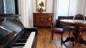 A piano, a wooden cabinet with a mirror, a red chair, and a round table with a glass top. - Roma Room Hotel (Rome)